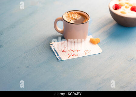 Tasse arabischen Kaffee und ein Herz, Zucker auf Mathe Papier mit der Liebe Sie Nachricht und eine Schale mit Joghurt auf einem blauen Holztisch, morgens li Stockfoto
