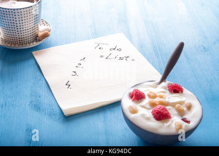 Tasse arabischen Kaffee, eine Schale Joghurt mit Himbeeren und Müsli und eine Serviette mit einem, um Liste zu tun, auf einem blauen Holztisch. Stockfoto