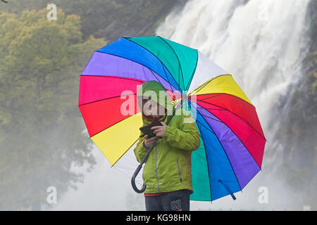 Junge mit Smartphone und Regenschirm vor der Powerscourt Wasserfall, Bray, Co Wicklow, Irland Stockfoto