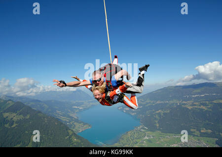 Dieses Tandem skydiving Paar fällt sich über einen schönen Berge und den See. Glück ist auf die smiley-Gesichter zu sehen. Stockfoto