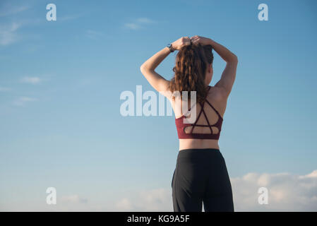 Sportliche Frau ihr Haar Binden vor Beginn der Übung und Ausbildung das Tragen eines Sport-BH, Ansicht von hinten. Stockfoto