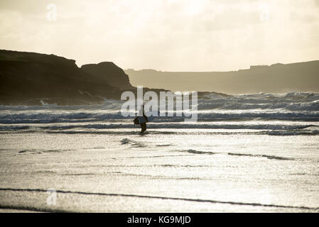 Starke Winde und kalten Wetter an der Küste von North Cornwall in hellen Herbst Sonnenschein an Polzeath, Cornwall, UK. Ein Surfer trotzt der Kälte und bereitet die Wellen in Angriff zu nehmen. Stockfoto