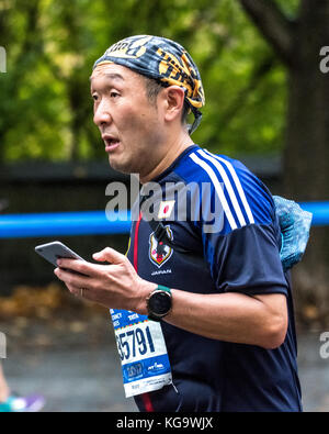 New York, USA. Nov. 2017. Jun Nakakima aus Setagaya-Ku, Japan, überprüft sein Handy, während er beim New-York-City-Marathon durch die Fifth Avenue läuft. Kredit: Enrique Shore/Alamy Live News Stockfoto