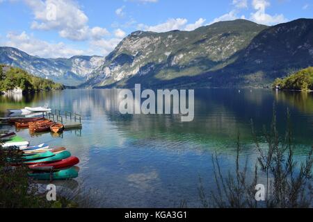 Boote am Ufer des Sees von Bohinj und der Himmel und die Berge im See spiegeln Stockfoto