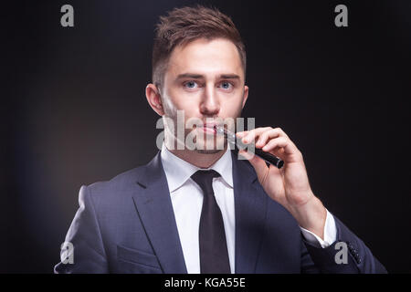 Bild von ernsthaften Geschäftsmann stehend mit vaping Gerät Stockfoto
