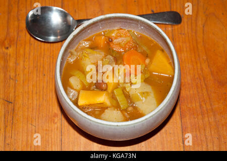 Schüssel mit rustikalen, chunky Gemüse und Bohnen Suppe/Eintopf, serviert auf einem Holztisch Stockfoto