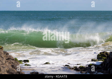 Indischen Ozean Wellen auf Basalt Felsen am Meer Strand Bunbury Western Australia an einem sonnigen Morgen in der Mitte brechen - Winter sendet salzige Gischt hoch. Stockfoto