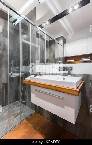 Graues Badezimmer mit weißem Waschbecken, Spiegel und begehbarer Dusche Stockfoto
