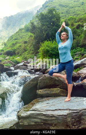 Frau in Yoga Asana Vrikshasana Baum am Wasserfall im Freien Stockfoto
