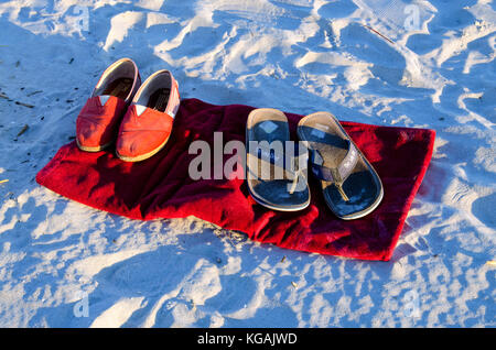Barfuß am Strand. Sandalen auf dem Handtuch auf dem Sand gelassen, als Strandgänger beschließen, den Strand barfuß zu erleben. Stockfoto