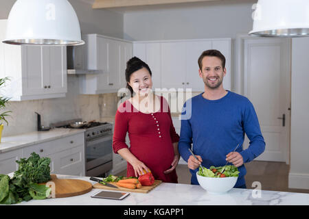 Lächelnd schwangeren Paare Vorbereitung Salat in der Küche Stockfoto
