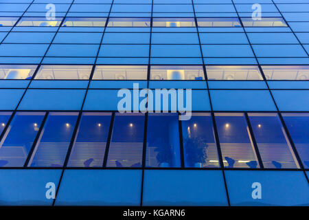 Blau gefärbte Bürofassade mit geometrisch gemusterten Fenstern und warmer Innenbeleuchtung, London, Großbritannien Stockfoto