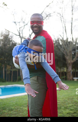 Sohn und Vater vorgibt, ein Superheld im Garten zu sein Stockfoto