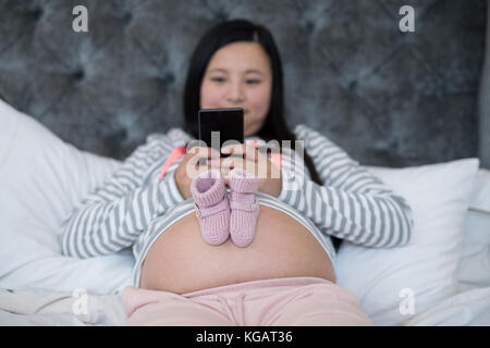 Paar Baby Socken auf Bauch schwangerer Frauen im Schlafzimmer Stockfoto