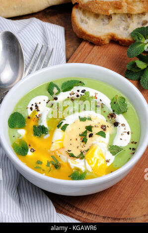 Erbsenpüree Suppe mit pochiertem Ei, saure Sahne, Minze gewürzt mit Gewürzen. Stockfoto