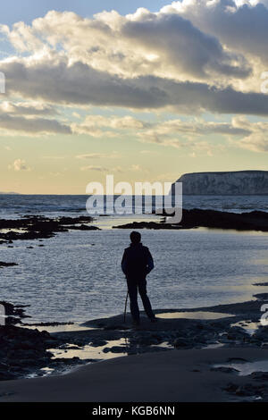 Ein Mann stand allein auf dem Meer oder am Strand mit Blick auf das Meer in Silhouette gegen einen Abend Himmel oder den Sonnenuntergang. felsige Küstenlinie, Isle of Wight. Stockfoto