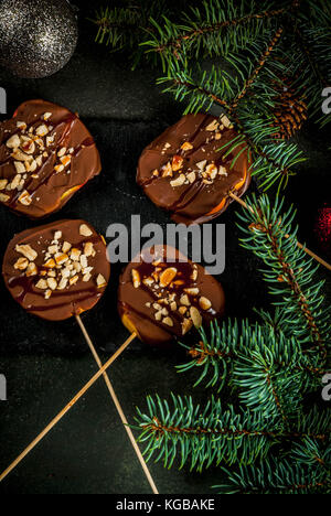 Ideen von Winter, Weihnachten behandelt. Süßigkeiten für Kinder. Schokolade Apfelscheiben in Schokolade, Karamell und Muttern. dunkelgrünen Hintergrund, Witz Stockfoto