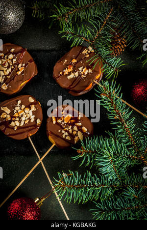 Ideen von Winter, Weihnachten behandelt. Süßigkeiten für Kinder. Schokolade Apfelscheiben in Schokolade, Karamell und Muttern. dunkelgrünen Hintergrund, Witz Stockfoto