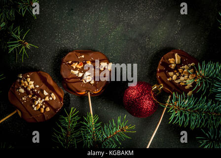 Ideen von Winter, Weihnachten behandelt. Süßigkeiten für Kinder. Schokolade Apfelscheiben in Schokolade, mit Karamell und Muttern. dunkelgrünen Hintergrund, mit Stockfoto