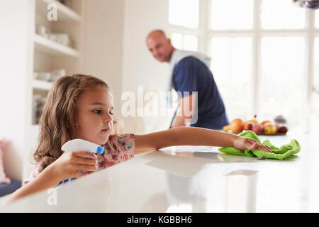 Junge Mädchen Reinigung Küche Arbeitsplatte, Papa im Hintergrund Stockfoto