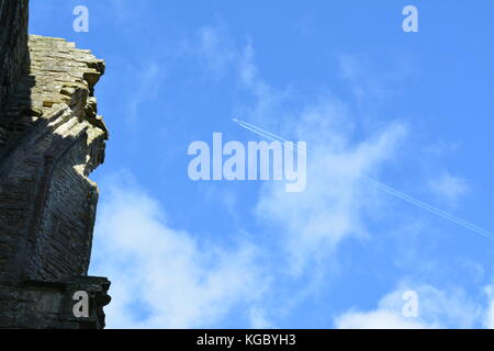 Sonnig herbstlichen blauer Himmel mit dünnen Wolken übersicht Verkehrsflugzeug und Kondensstreifen flogen über den Ruinen des alten Klosters Tintern Abbey monmouthshire Stockfoto