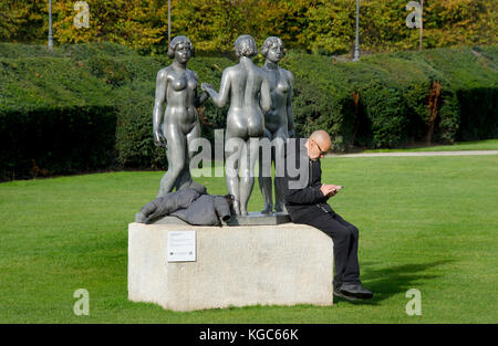 Paris, Frankreich. Jardin des Tuileries: Les Nymphes / Trois Grâces (drei Grazien) von Aristide Maillol, 1938. Mann mit Handy Stockfoto