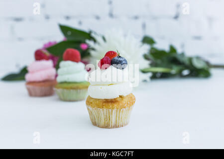 Verschiedene Cupcakes mit frischen Beeren Blumen und Blätter. weißen Hintergrund. Stockfoto