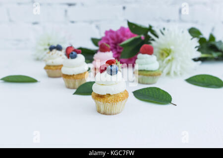 Verschiedene Cupcakes mit frischen Beeren Blumen und Blätter. weißen Hintergrund. Stockfoto