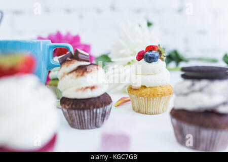 Cupcakes mit frischen Beeren Blumen und Blätter, eine Tasse Kaffee oder Tee die weißen Hintergrund. Stockfoto