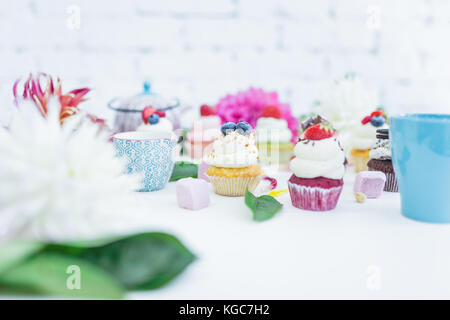 Cupcakes mit frischen Beeren Blumen und Blätter, eine Tasse Kaffee oder Tee die weißen Hintergrund. Stockfoto