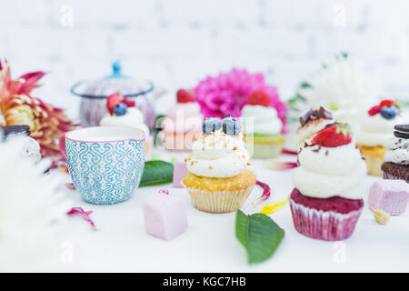 Cupcakes mit frischen Beeren Blumen und Blätter, eine Tasse Kaffee oder Tee die weißen Hintergrund. Stockfoto