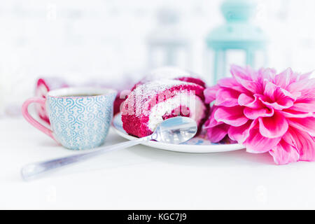 Eine Red Velvet Cake roll geschnitten bei einer Tasse Kaffee oder Tee und Blumen. weißen Hintergrund. Stockfoto