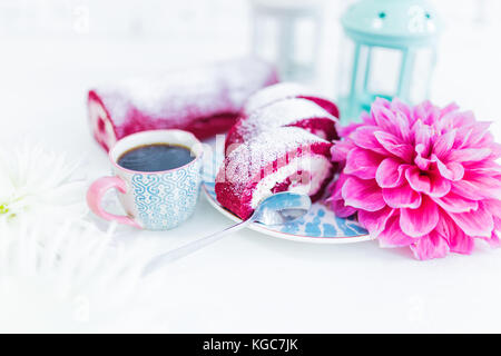 Eine Red Velvet Cake roll geschnitten bei einer Tasse Kaffee oder Tee und Blumen. weißen Hintergrund. Stockfoto