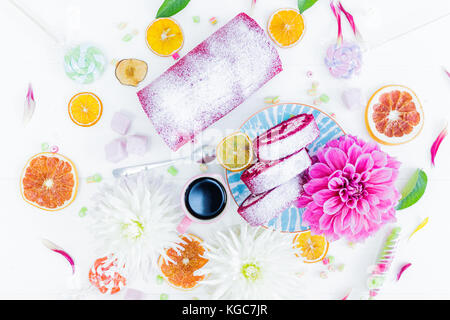 Eine Red Velvet Cake roll geschnitten mit Tasse Kaffee Blumen und Süßigkeiten, getrocknete Orangen. top anzeigen. weißen Hintergrund. Stockfoto