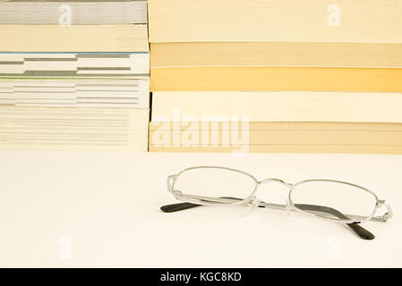 Stapel Bücher Romane auf einem weißen reflektierenden Oberfläche mit etwas Silber Gläser (Brille) im Vordergrund liegen. Lesekompetenz Konzept Stockfoto