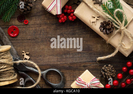 Weihnachten - Weihnachtsgeschenk in braunes Packpapier eingewickelt, sackleinen Garn, vintage Schere, rote Tasten, Rentiere, Tannenzweigen und Tannenzapfen. Flach, über Stockfoto