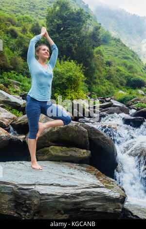 Frau in Yoga Asana Vrikshasana Baum am Wasserfall im Freien Stockfoto