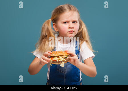 Adorable kleine süße Mädchen in weißem Hemd und Jeans Overall mit Hamburger Stockfoto