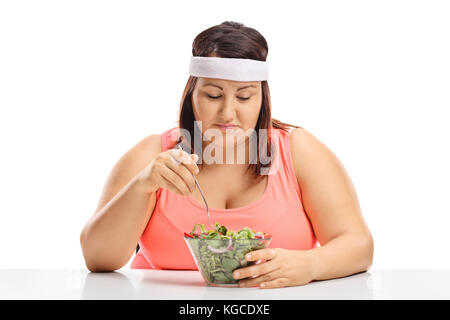 Traurig übergewichtige Frau an einem Tisch sitzen und auf eine Schüssel Salat auf weißem Hintergrund Stockfoto