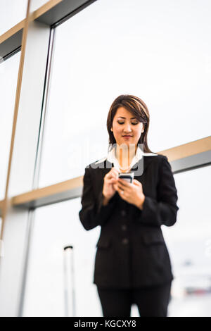 Eine asiatische Geschäftsfrau Textnachrichten auf Ihrem Smartphone beim Warten auf ein Flugzeug Abflug. Stockfoto