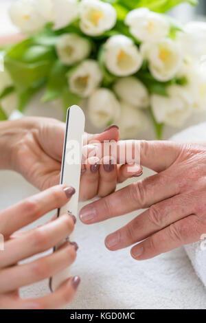Nahaufnahme der Hand eines qualifizierten Maniküre Feilen der Nägel, einer jungen Frau mit einem weißen Puffer in einem trendy Nail Salon Stockfoto