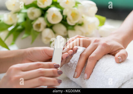 Nahaufnahme der Hand eines qualifizierten Maniküre Feilen der Nägel, einer jungen Frau mit einem weißen Puffer in einem trendy Nail Salon Stockfoto