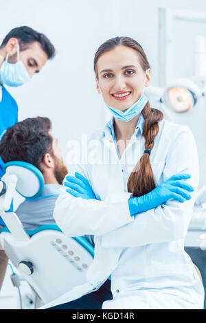 Portrait eines glücklichen und selbstbewussten weiblichen Zahnarzt Tragen von sterilen weißen Mantel- und OP-Handschuhe, während die Kamera in der Zahnarztpraxis eines mod suchen Stockfoto