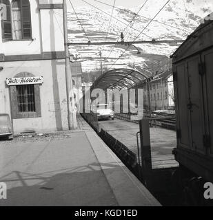 1950er Jahre, historische Bild von Autos auf der open-air-Waggons eines Autotransporter Zug (Autoverlad) Ankunft in Meran in Südtirol, Italien. Dies war eine beliebte Methode, um den Transport von Personen und Fahrzeugen in Europa zu dieser Zeit. Stockfoto