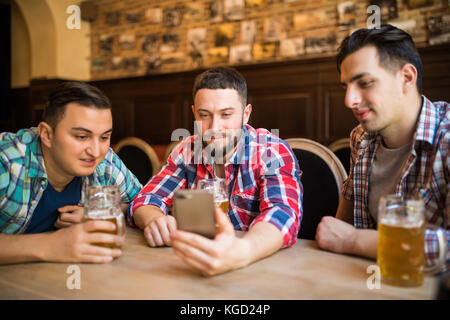 Freundliche alte Freunde Spaß mit Smartphone und trinken Bier im Pub. Stockfoto
