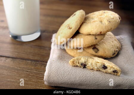 Auswahl von Choc Chip und Obst Plätzchen, auf einer Serviette, mit einem Glas Milch auf einem Holztisch Stockfoto