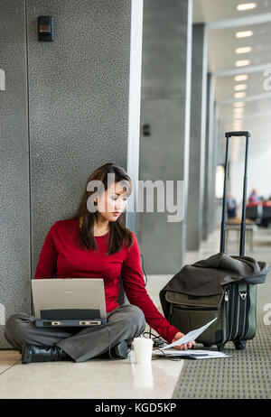 Eine Geschäftsfrau auf dem Fußboden sitzen an Ihrem Abfluggate an einem Flughafen arbeiten an Ihrem Computer. Stockfoto