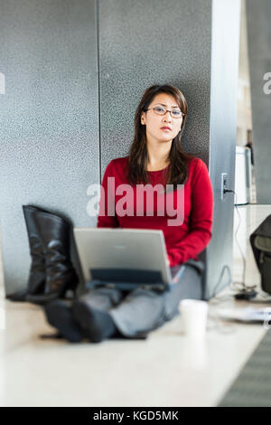 Eine Geschäftsfrau auf dem Fußboden sitzen an Ihrem Abfluggate an einem Flughafen arbeiten an Ihrem Computer. Stockfoto