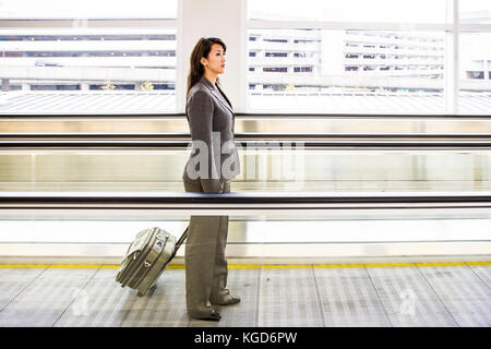 Eine Geschäftsfrau auf dem Bürgersteig in einem Flughafen mit Ihrem rollenden Gepäck. Stockfoto