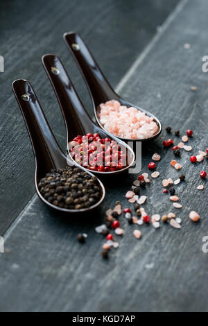 Studio shot von drei Löffel mit groben Salz Rosa, Schwarz und rosa Pfeffer auf dunklem Hintergrund Stockfoto
